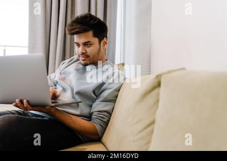 Young indian man workong with laptop sitting on sofa at home Stock Photo