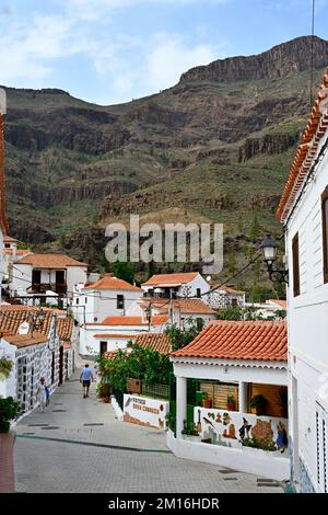 Small narrow street in the mountain village of Fataga with red tiled roofs and rugged mountains behind, Gran Canaria Stock Photo