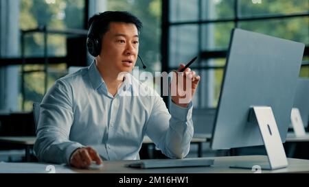 Chinese male asian mature businessman consultant office manager korean man in headphones communicate online use computer video call application take Stock Photo