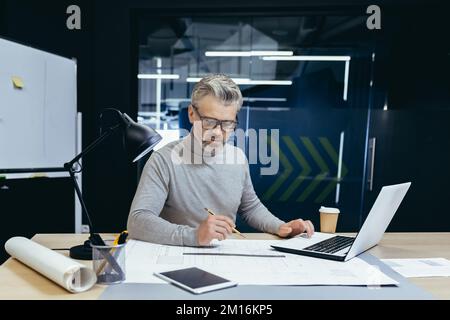 Serious thinking architect designer working on blueprint, mature man working inside office engineer designing on whatman. Stock Photo