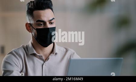 Arabian sick businessman in medical mask designer programmer typing on laptop search information in network develop startup project chatting in online Stock Photo