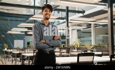 Confident smiling indian young man guy businessman investor founder salesman manager make crossed arms stand in office handsome adult male analyst dir Stock Photo