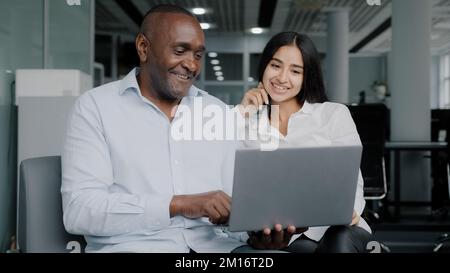 Diverse colleagues two business partners african arabian co-workers discuss internet project on laptop at office meeting planning working main tasks p Stock Photo