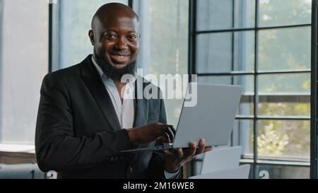 Businessman american african entrepreneur ceo analyst investor stand in modern skyscraper office hold laptop work in marketing department e-commerce o Stock Photo