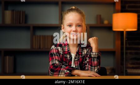 Overjoyed beautiful little young baby pupil in shirt posing clenching doing yes hand gesture. Girl wins competition achieves goal makes triumph symbol Stock Photo