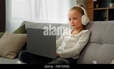 Relaxed funny pupil girl wearing headphones using laptop greeting classmates in video conference call talking online with teacher remotely via webcam Stock Photo