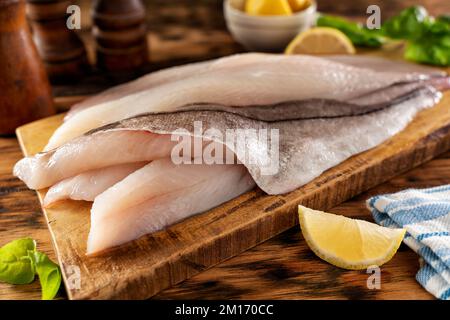 Fresh haddock fillets on a rustic cutting board with lemon and herbs. Stock Photo