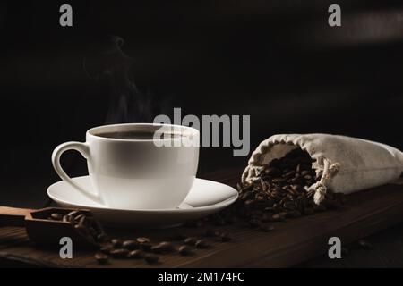 White cup of fresh hot coffee and coffee beans on wooden board on table. Stock Photo