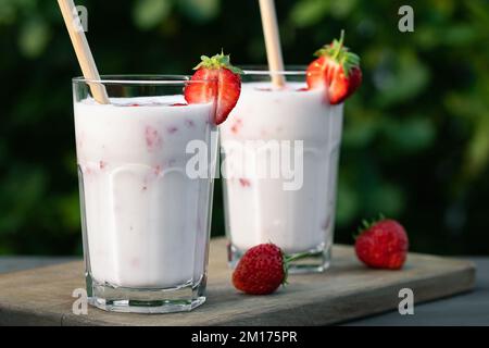 Strawberry smoothie in two glass glasses and fresh strawberries on a wooden table in the yard. Stock Photo