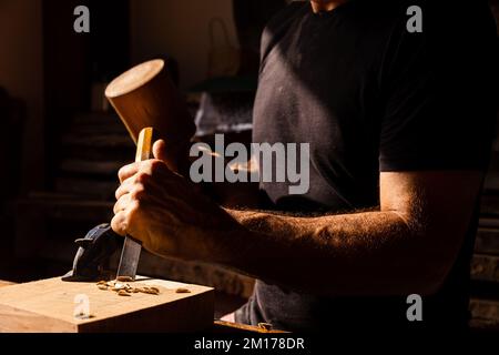 A close up of man's hands using a chisel and a mallet on a piece of wood - concept of crafts Stock Photo