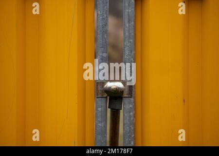 Closeup of a hole between two segments of a modular construction site fence. The segmaents are orange and are connected with a metal support. Stock Photo
