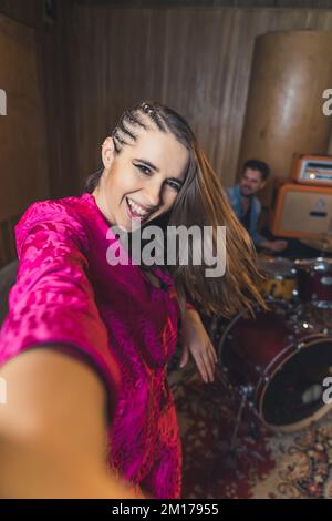 joyful young singer in pink clothes taking a selfie with a drummer, musical studio. High quality photo Stock Photo