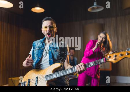 music band performing in a recording studio, bass guitarist in front and a singer and a drummer in the background music band concept. High quality photo Stock Photo