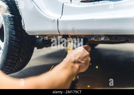 Equipment needed in mechanical work. Car repair process. Low angle indoor shot of caucasian arm without protection using grinder to cut into metal chassis. High quality photo Stock Photo