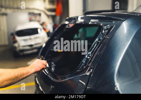 Inside mechanic's garage. Hand of a caucasian man removing glue residues before the installing process of new rear window in a black car. High quality photo Stock Photo