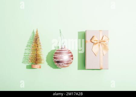 Gift box, Christmas ball and fir tree toy on green background with sharp shadows. Minimal composition. Top view, flat lay. Stock Photo