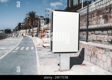 A vertical rectangular white empty advertising billboard template on the sidewalk; a mock-up of a blank advert poster placeholder in the pedestrian wa Stock Photo