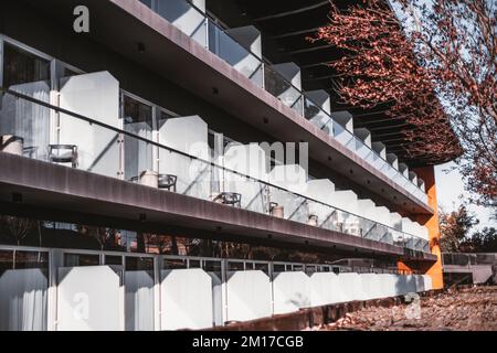 A perspective view of a facade of a modern hotel in a tourist resort with rows of glass-fenced balconies and chairs on them making a pattern, windows; Stock Photo