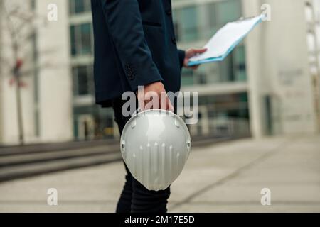 Close up of engineer in suit holding protective helmet and paper folder. Industrial concept Stock Photo