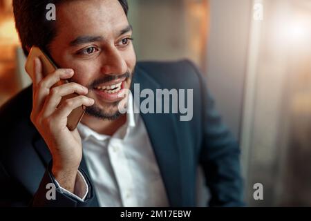 Close up of smiling indian businessman talking by phone with client. Blurred background Stock Photo