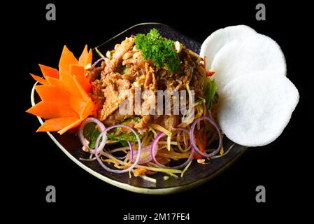 Asian beef salad with green papaya served with rice chips isolated on black background side view Stock Photo