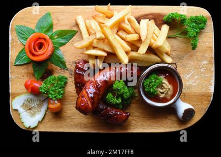 Fried sausages with french fries and spicy sauce on wooden board isolated on black background side view Stock Photo