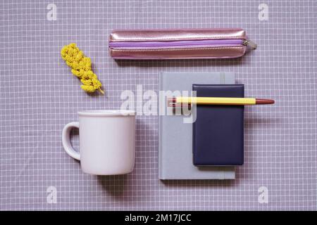 Stationery, office supplies. Notebook, pen, mug cup, pencil case on purple check pattern fabric background. flat lay, top view Stock Photo
