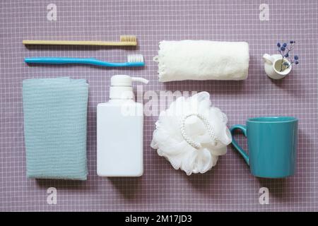 Bathroom spa shower products. toothbrush, towel, shampoo soap bottle, cup on purple check pattern fabric background. flat lay, top view Stock Photo