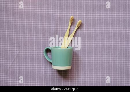Bamboo wood toothbrush in mint color cup on purple check pattern fabric background. top view Stock Photo