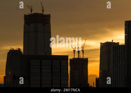 Mount Fuji seen behind the silhouettes of skyscrapers being built in Tokyo at sunset. Tokyo, Japan. Stock Photo
