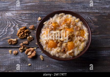 Delicious oatmeal porridge with baked pumpkin, honey and nuts in ceramic bowl on wooden table. healthy homemade breakfast. selective focus Stock Photo