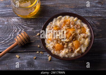 Delicious oatmeal porridge with baked pumpkin, honey and nuts in ceramic bowl on wooden table. healthy homemade breakfast. selective focus Stock Photo