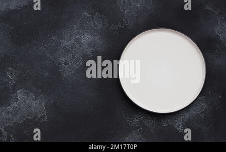 White plate on black textured background, top view, space Stock Photo