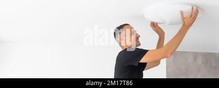 Worker repairing lamp on stretch ceiling indoors Stock Photo