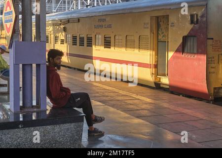 A young Indian man, a railway passenger, sitting in front of a long-distance train at Chhatrapati Shivaji Maharaj Terminus in Mumbai, India Stock Photo