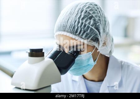 Portrait of female bio engineer looking in microscope while working in scientific laboratory Stock Photo