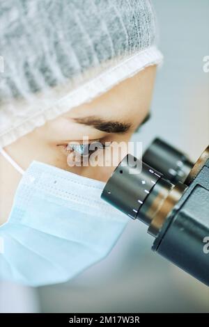Vertical closeup of young female medic looking in microscope while working with test samples in laboratory Stock Photo