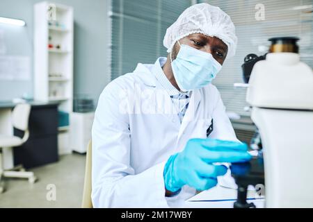 Portrait of focused black man wearing face mask while doing research in medical laboratory Stock Photo
