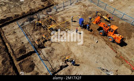 Aerial view excavator and construction workers working on construction site in open field. Pipe laying in trench for gasification. Top point of shooting. Repair and restoration of natural gas supply.. Stock Photo