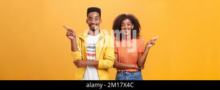 Which one telling true. Joyful and friendly good-looking couple, african american woman pointing left and dark-skinned guy right smiling broadly at Stock Photo