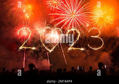 2023 new year text made with fireworks sparklers and bengal lights on night sky at midnight. Crowd of People celebrate, concert stage and hands up in Stock Photo