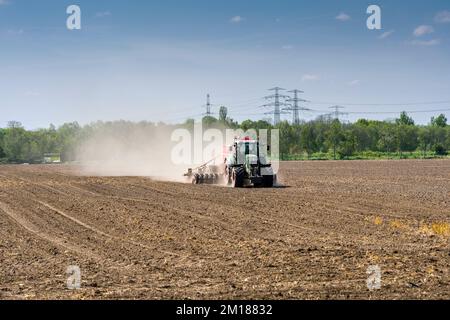 Agricultural landscape with a tractor ploughing a field, trees and overhead powerlines Stock Photo