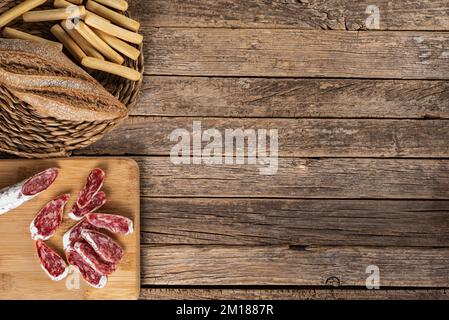 Fuet, typical Catalan sausage spread throughout Spain based on pork and bacon, cut into slices on a wooden cutting board and some buns. Stock Photo