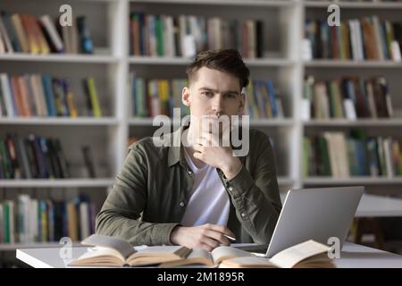 Serious handsome college student writing essay in university library Stock Photo