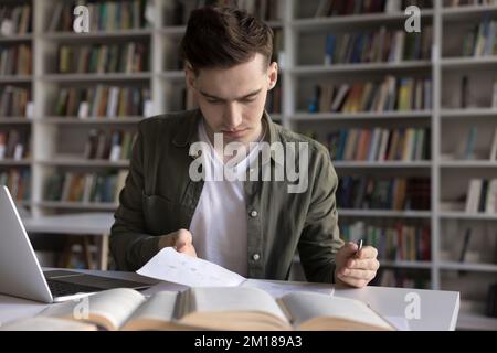 Focused serious student guy writing webinar summary, reading notes Stock Photo