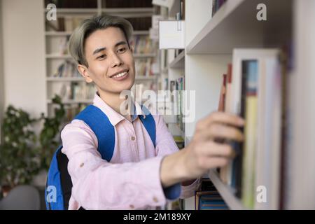 Happy Asian teen student guy choosing literature in university library Stock Photo