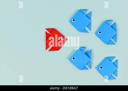 Paper fish swimming swimming against the current in other direction than different colored fish Stock Photo