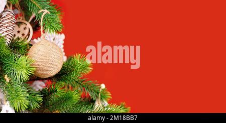 Banner with Christmas tree branches with natural ornament bauble made from beige jute rope on red background Stock Photo
