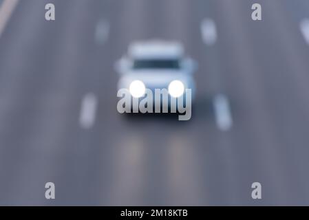 Defocused car on the highway with headlights on between the median lanes. Stock Photo