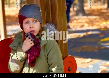 Offended frightened child in a jacket and a hat on an autumn playground Stock Photo